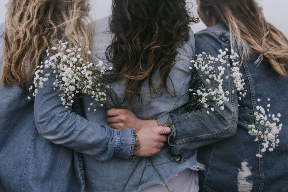 Frauen von hinten mit Jeans-Jacken und Schleierkraut in den Händen umarmen sich