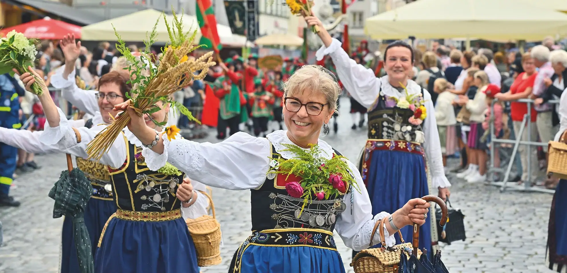 Traditionell gekleidete Frauen beim Festumzug, die in die Kamera grinsen
